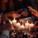 Plusieurs personnes sont assises autour d'une table, éclairées par la lumière chaleureuse de bougies. Elles sont plongées dans leurs smartphones, illustrant l'impact de la mort sur les interactions sociales et la communication dans l'ère numérique