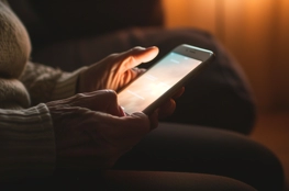 Une personne tenant un smartphone dans un environnement sombre, recherchant des groupes de soutien en ligne pour se connecter avec d'autres.