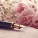 Un stylo-plume repose sur une lettre manuscrite, entouré de pivoines roses et de gypsophile, capturant l'essence intime et respectueuse de la rédaction et publication d'un avis de décès."