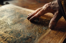 Une main âgée parcourt avec précaution la page ornée du Livre de Kells, révélant l'art insulaire complexe dans des tons de doré et de vert.