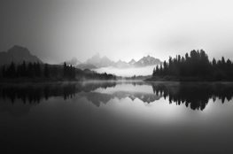 Un lac paisible reflétant des montagnes enneigées, sous une brume légère au lever du jour, offrant une atmosphère idéale pour ceux qui cherchent à commencer une méditation quotidienne.