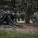 Dans ce cimetière ombragé, une statue voilée agenouillée évoque le deuil et la méditation devant les tombes des célébrités, un lieu où l'histoire et l'art funéraire se rencontrent.