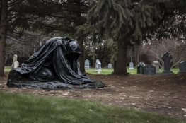 Dans ce cimetière ombragé, une statue voilée agenouillée évoque le deuil et la méditation devant les tombes des célébrités, un lieu où l'histoire et l'art funéraire se rencontrent.