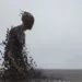 Fragmentation d'une sculpture humaine en bord de mer, illustrant le thème de la crémation comme processus de transformation et d’effacement du corps dans l’espace.