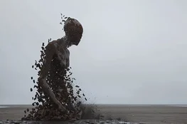 Fragmentation d'une sculpture humaine en bord de mer, illustrant le thème de la crémation comme processus de transformation et d’effacement du corps dans l’espace.