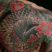 Tatouages commémoratifs représentant une carpe koi traditionnelle et des pivoines rouges couvrant l’épaule et le haut du dos d’une personne, illustrant un hommage durable à un défunt.