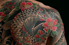 Tatouages commémoratifs représentant une carpe koi traditionnelle et des pivoines rouges couvrant l’épaule et le haut du dos d’une personne, illustrant un hommage durable à un défunt.