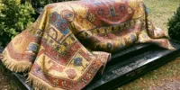 Sépulture de Rudolf Noureev recouverte d’un kilim oriental en mosaïque, photographiée dans un cimetière arboré. Le tombeau, en pierre noire, est orné de motifs colorés rappelant les tapis d’Orient.