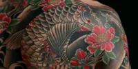Tatouages commémoratifs représentant une carpe koi traditionnelle et des pivoines rouges couvrant l’épaule et le haut du dos d’une personne, illustrant un hommage durable à un défunt.